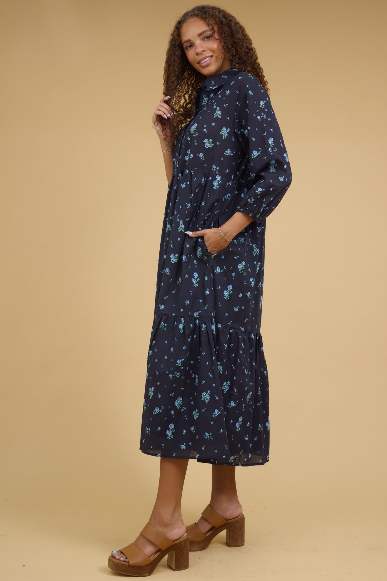 Back view of a  teenage girl wearing a navy midi dresswith long sleeves and side pockets.
