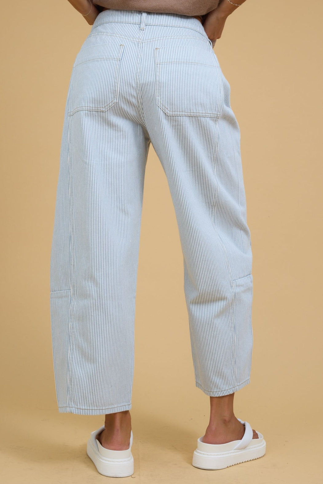 Back view of a woman wearing white & blue stripe, wide leg barrel jeans.