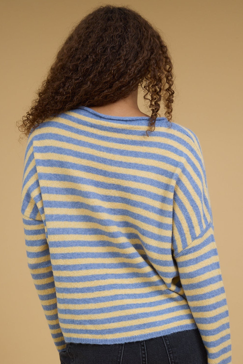 Back view of a woman wearing a yellow and lue stripe pullover with long sleeves.