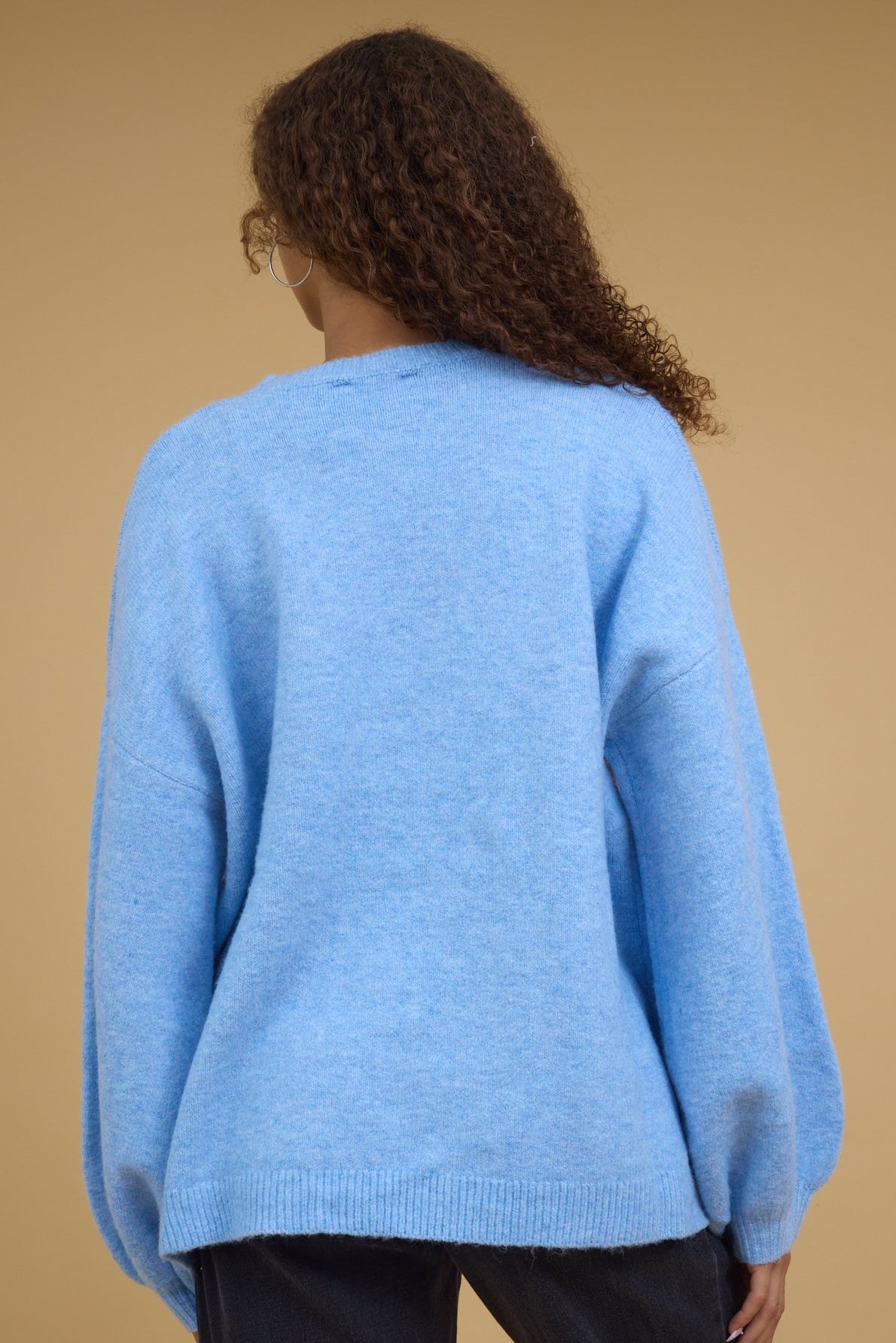 Back view of a young woman wearing a long sleeve, loose fittig sweater.