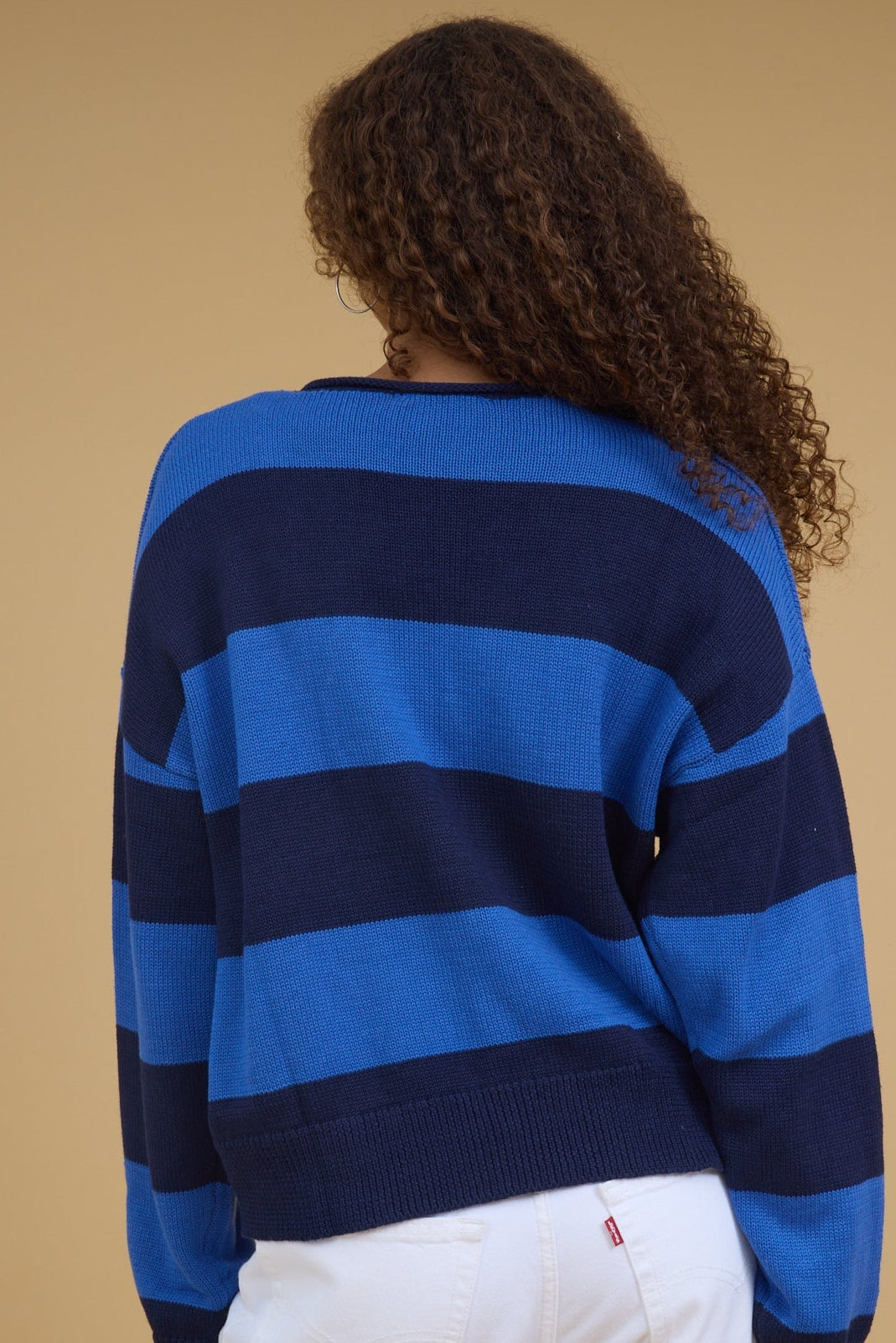 Back view of a woman wearing a wide stripe navy & blue stripe, long sleeve cardigan.