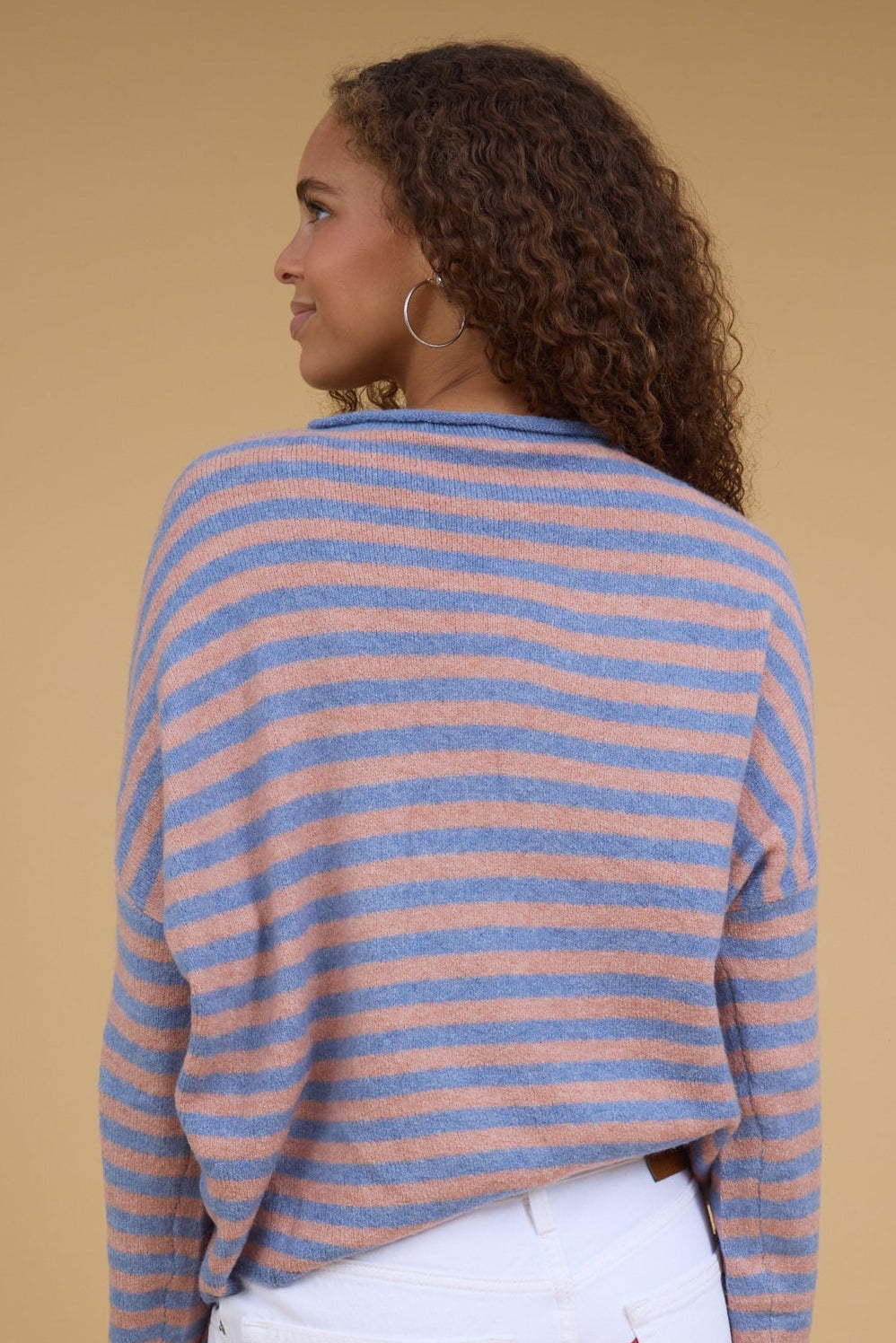Back view of a woman wearing a loose fitting long sleeve stripe sweater in blush & blue.