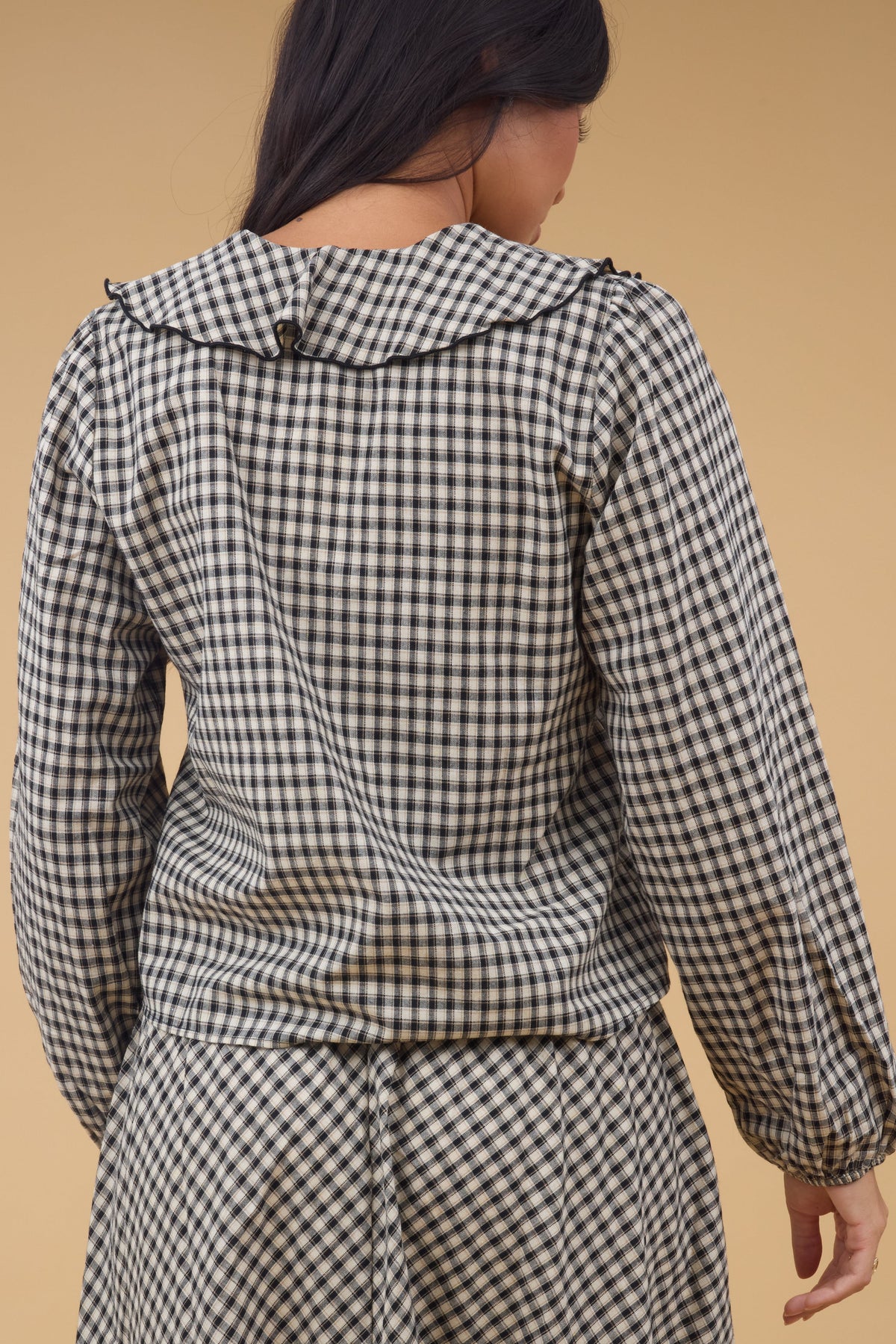 Back view of a woman wearing a black & tan plaid blouse with a ruffle collar and long sleeves.