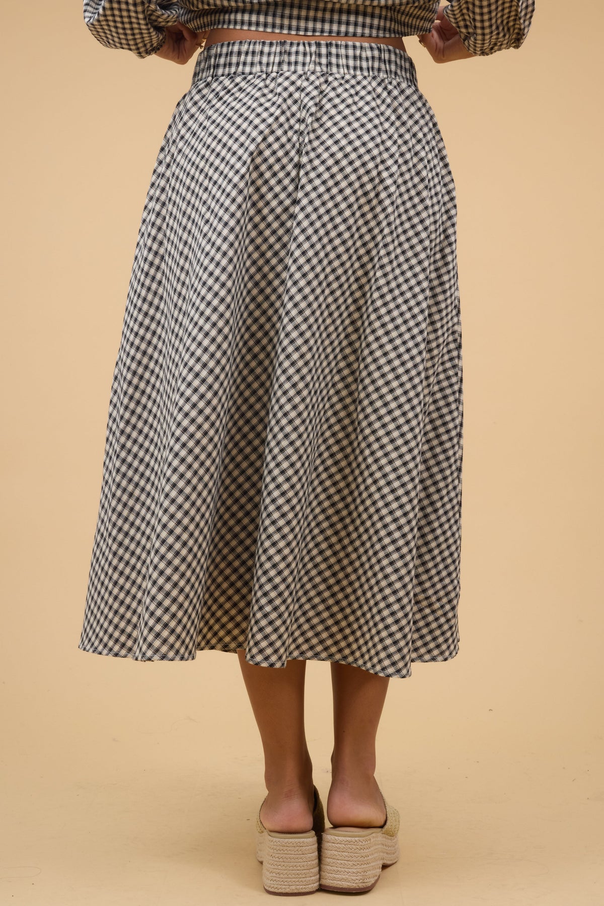 Back view of a woman wearing a tan & black plaid, A-line midi skirt wiht a wide elastic back waistband.