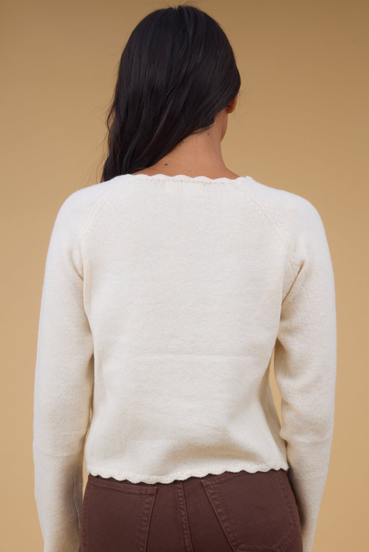 Back view of a woman wearing a slightly loose fitting cardigan with scallop hems.
