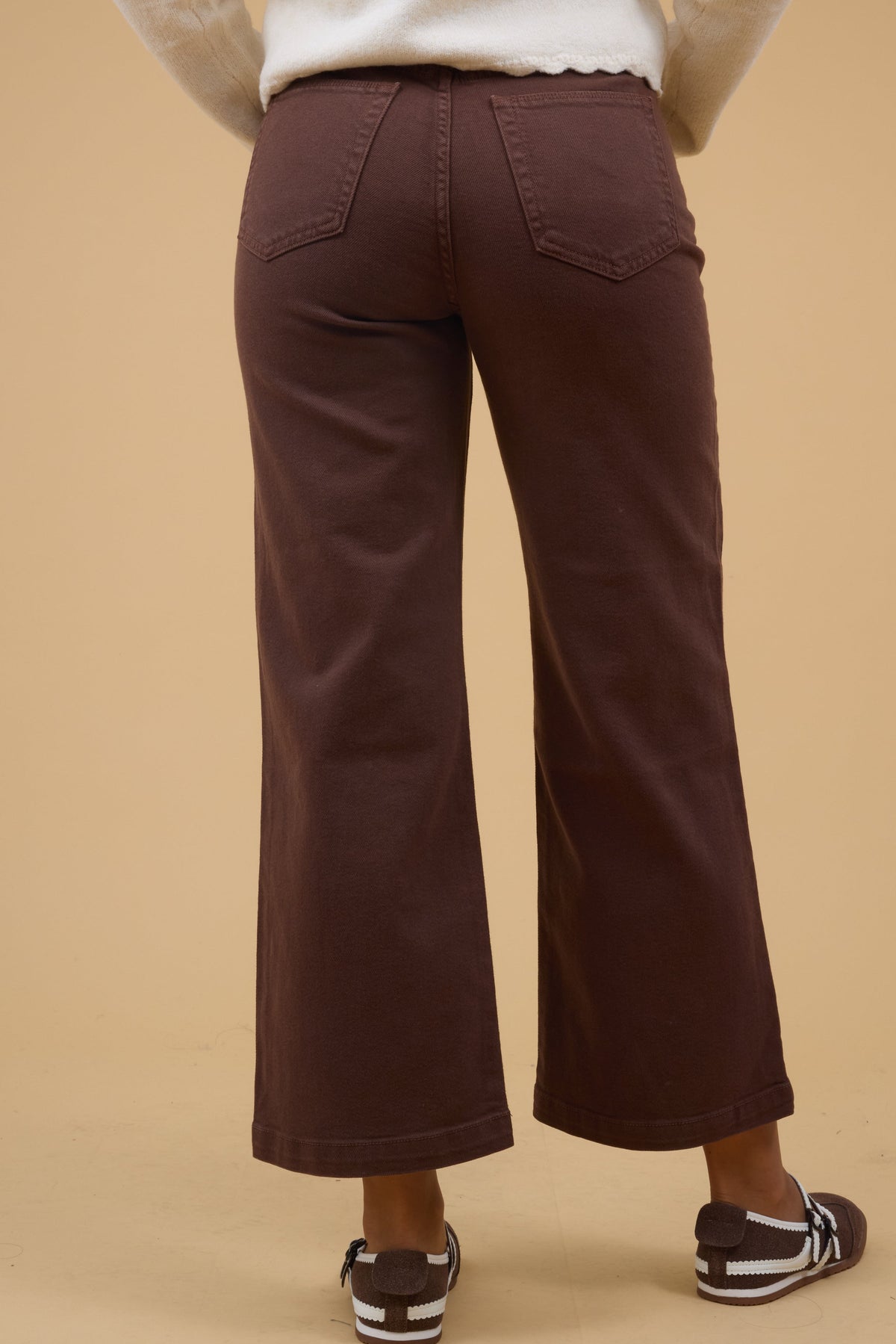 Back view of a young woman wearing a pair of brown, wide leg jeans and back pockets. 