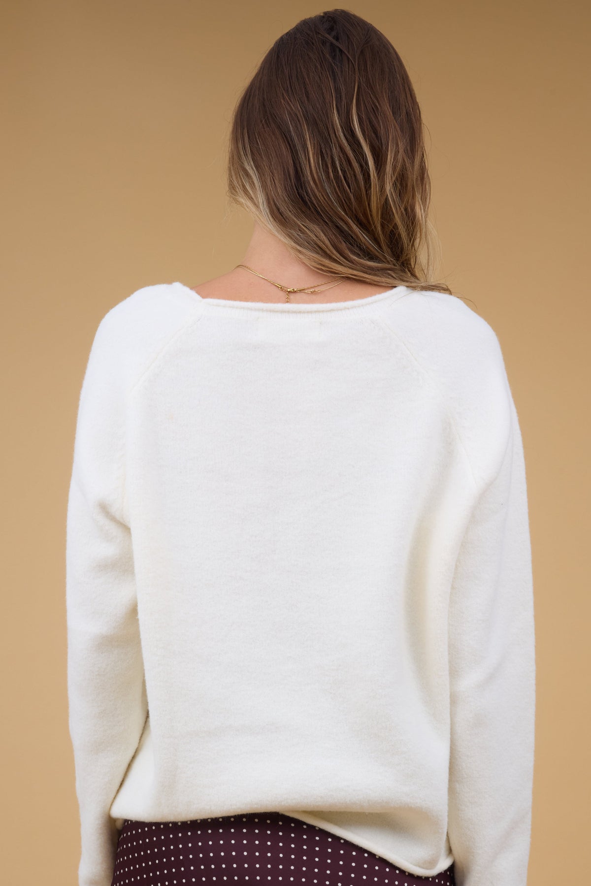 Back view of a woman wearing a cream, long sleeve sweater.