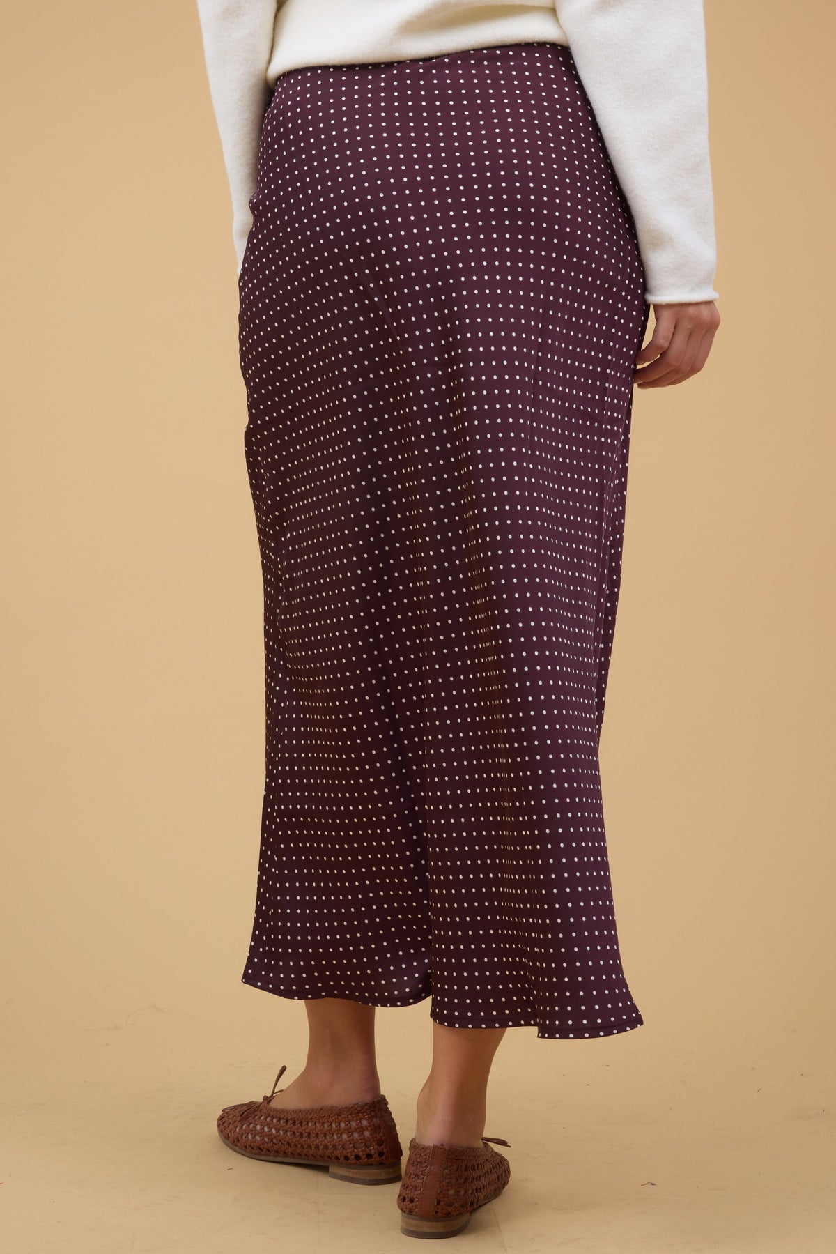 Back view of a woman wearing a brown with white polka dot midi skirt.