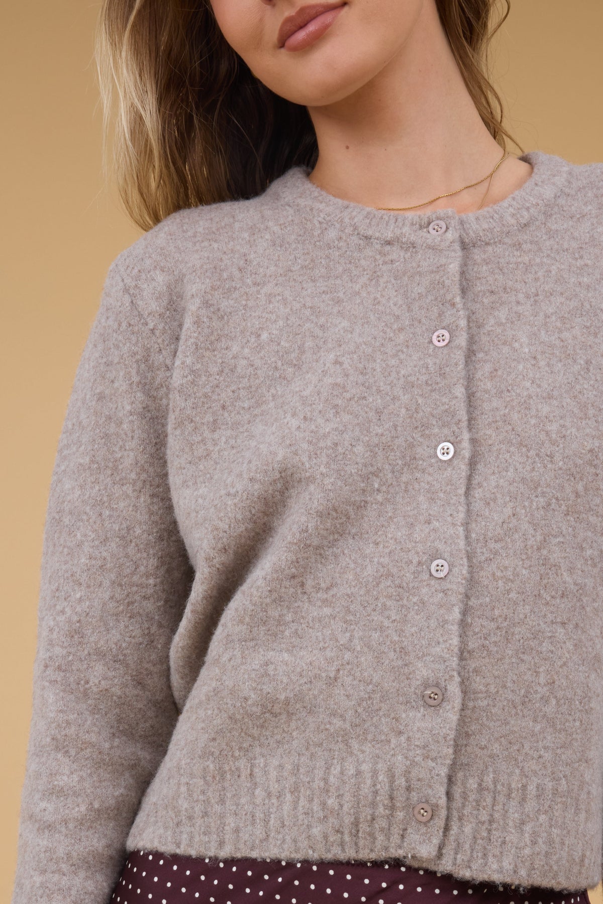 A close up view of a woman wearing a beige button down cardigan with matching buttons and long sleeves.