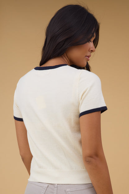 Back view of a woman wearing a cream top with black contrasting neckline and cuffs.