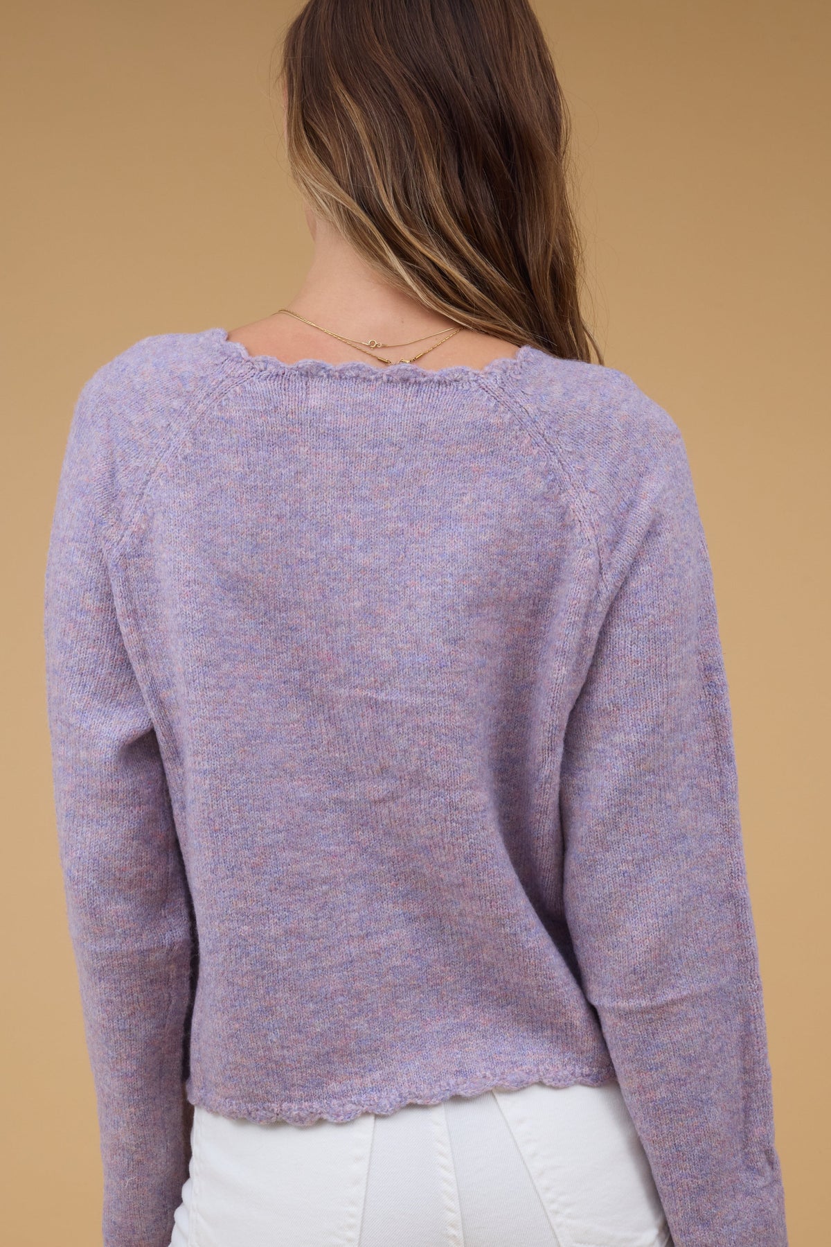 Back view of a woman wearing a lavender cardigan with scallop hems.