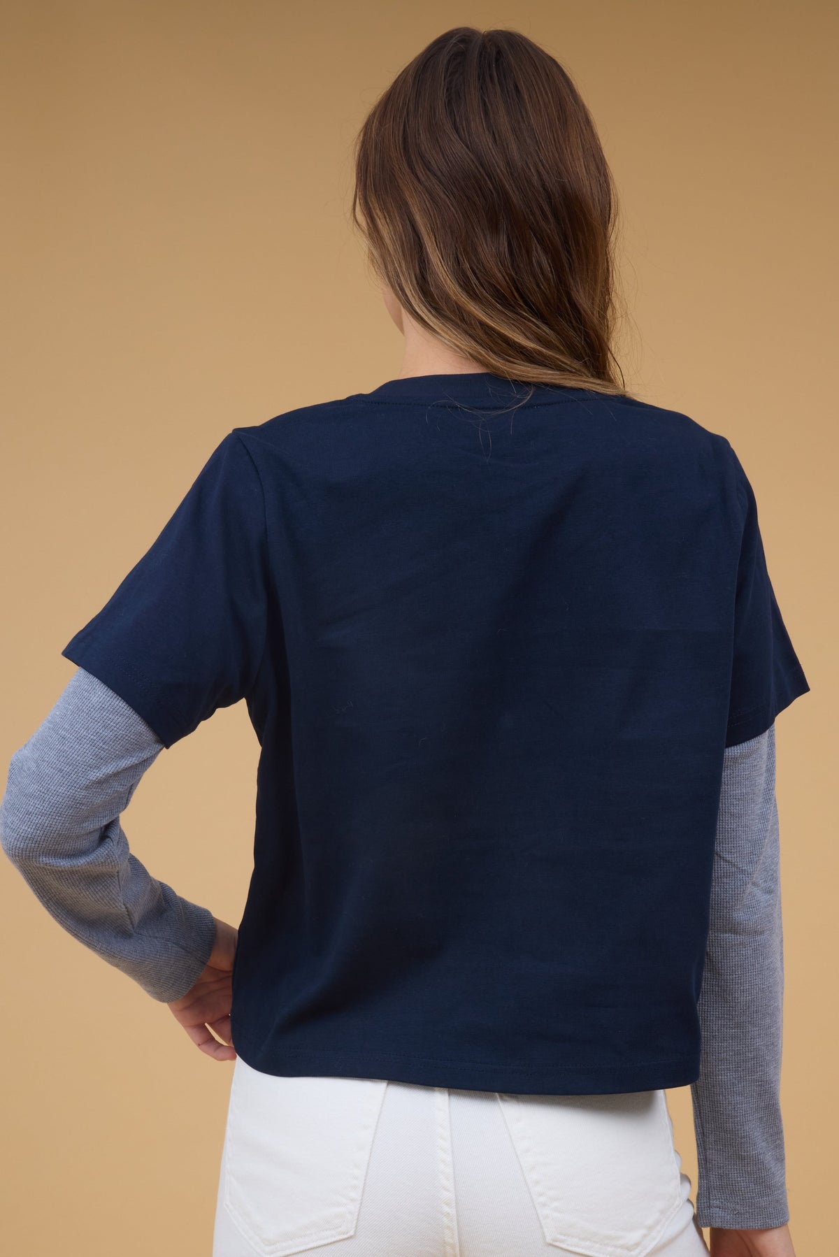 Back view of a woman wearing a long sleeve top with a navy short sleeve tee with attached, long waffle weave sleeves.