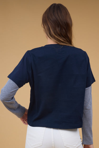 Back view of a woman wearing a long sleeve top with a navy short sleeve tee with attached, long waffle weave sleeves.