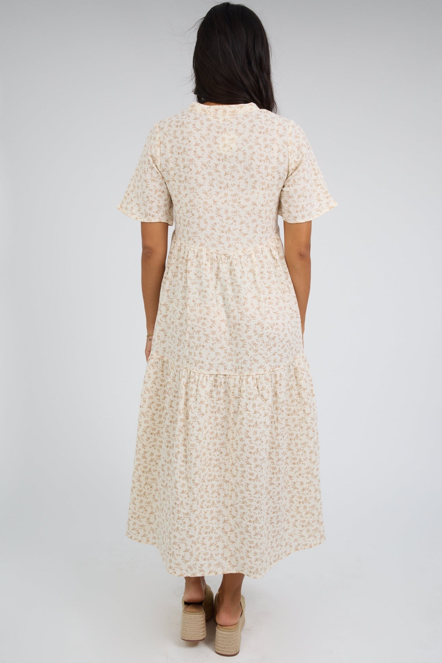 Back view of a woman wearing an ivory tiered midi dress with short sleeves.