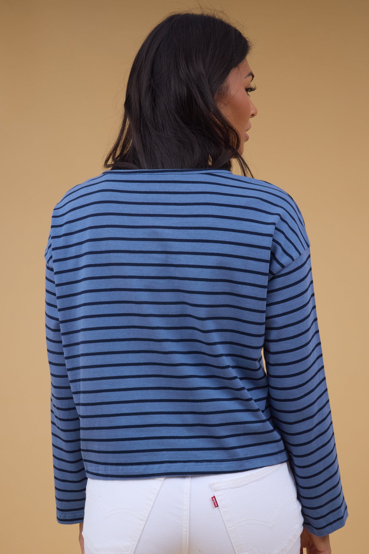 A back view of a woman wearing a loose fitting blue & navy stripe long sleeve tee.