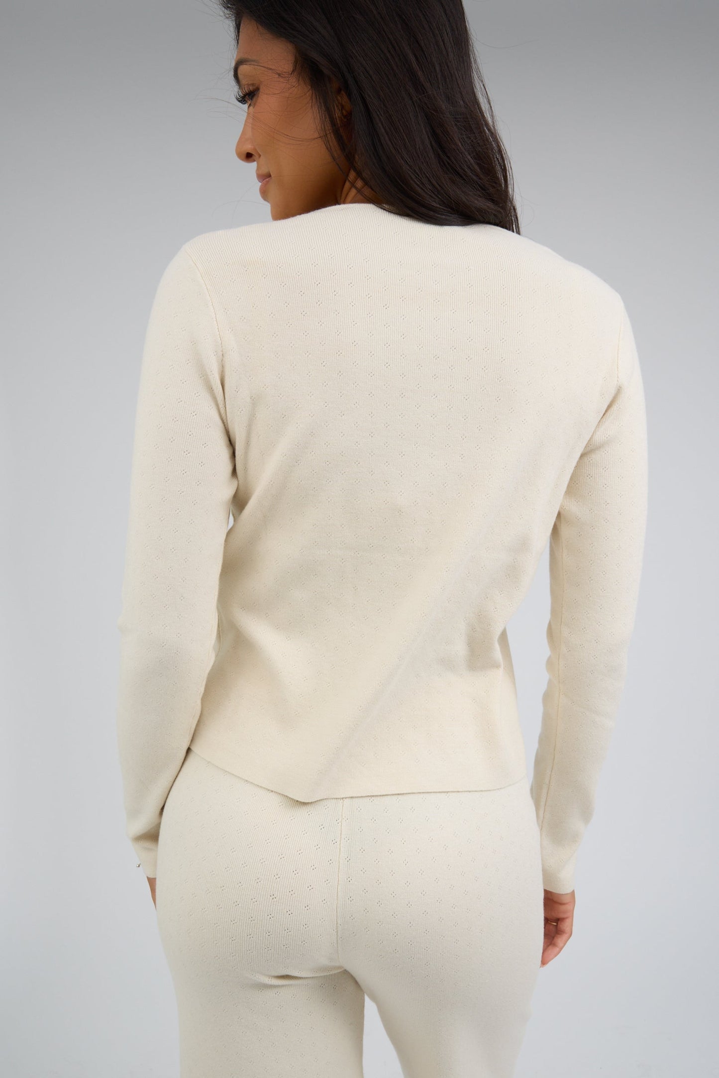 Back view of a woman wearing a cream pointelle knit outfit with long sleeves and an elastic waist.