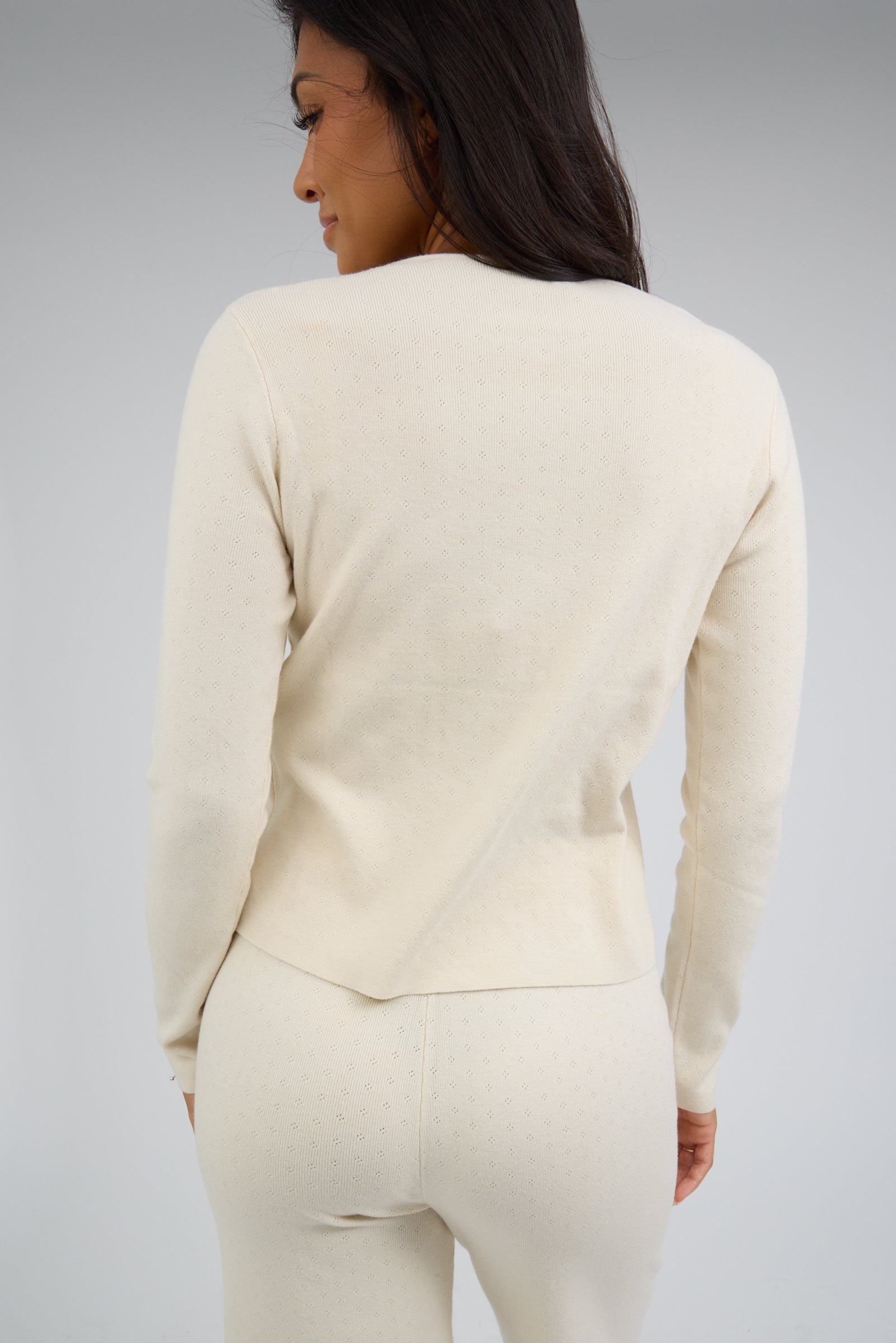 Back view of a woman wearing a cream pointelle knit outfit with long sleeves and an elastic waist.