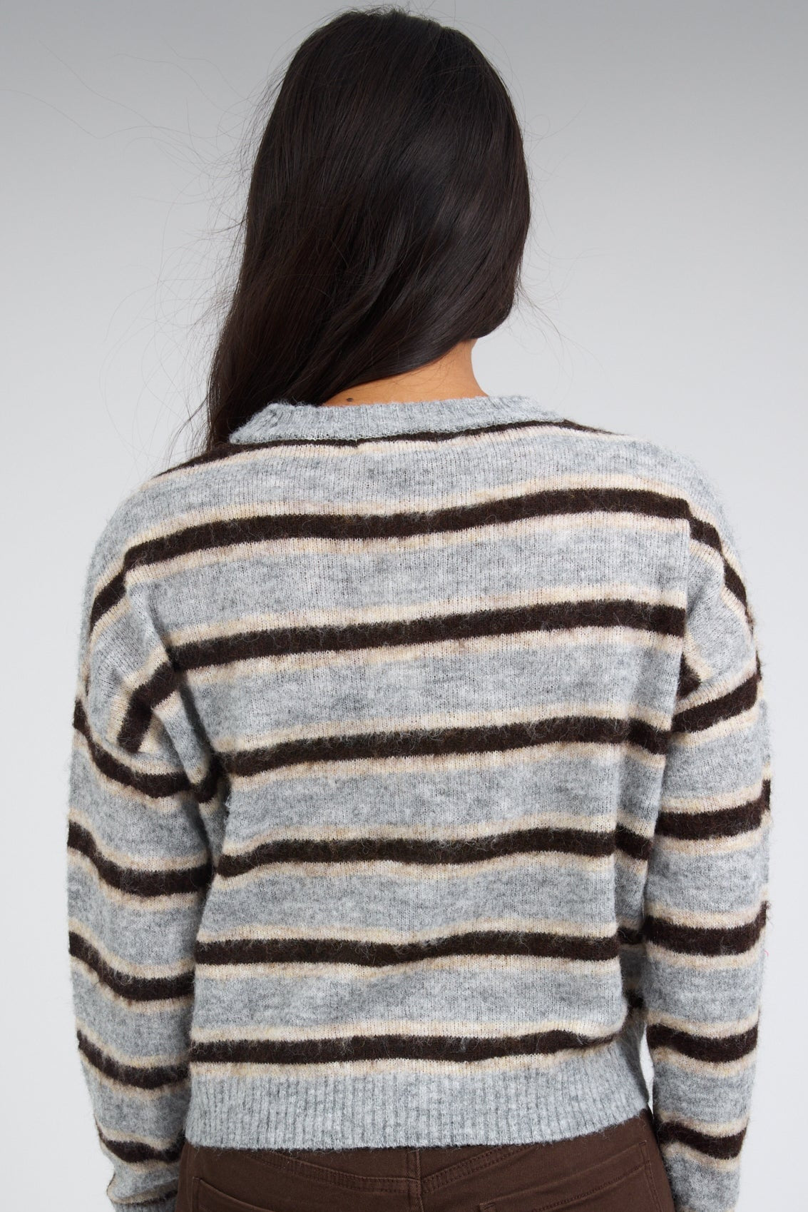 Back view of a woman wearing a grey & brown multi stripe long sleeve pullover.