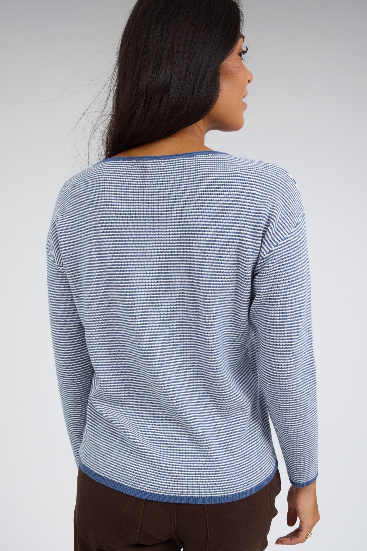 Back view of a young woman wearing a blue & white stripe top with long sleeves.