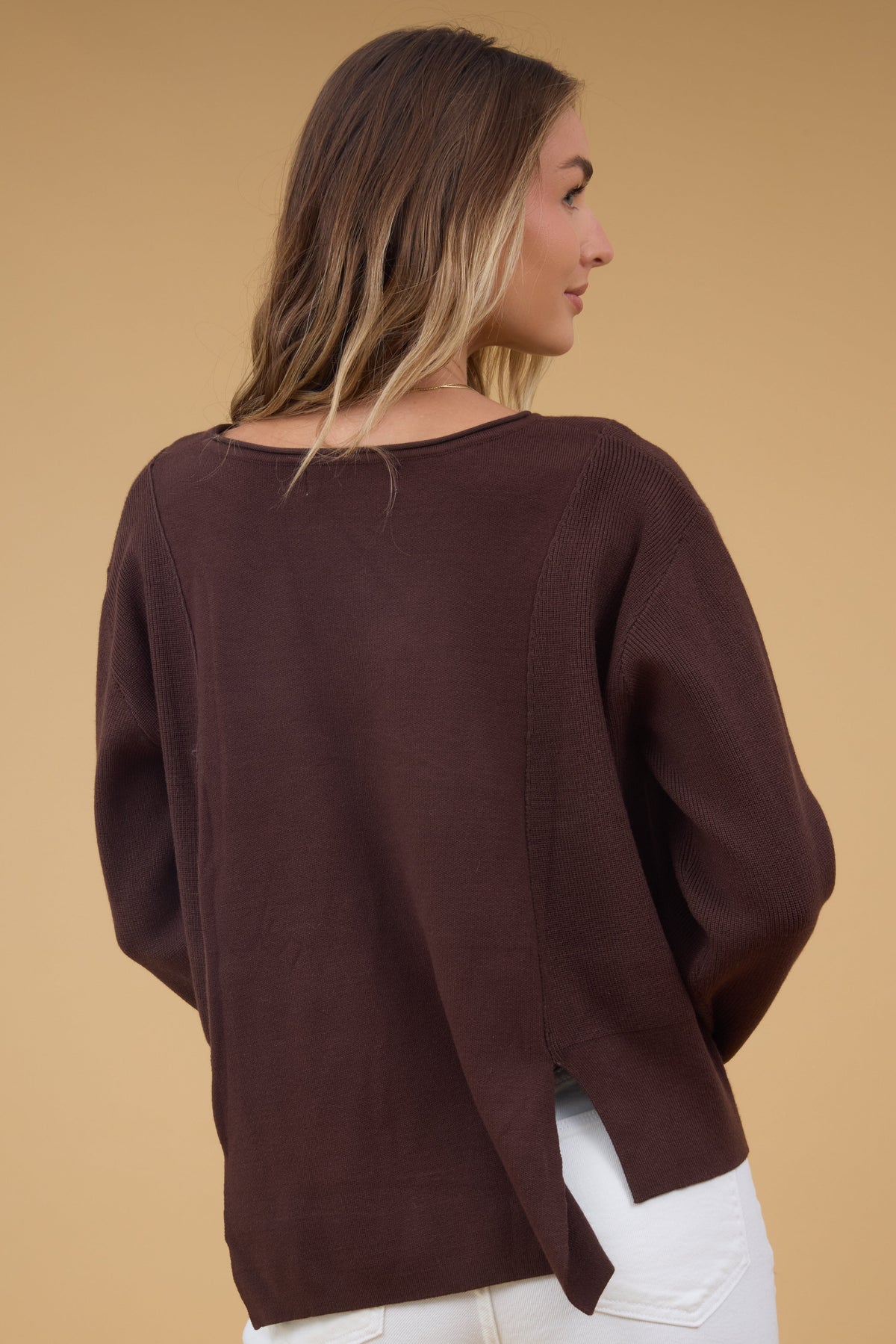 Back view of a woman wearing a loose fittig top with long sleeves and short slits  at the hips.