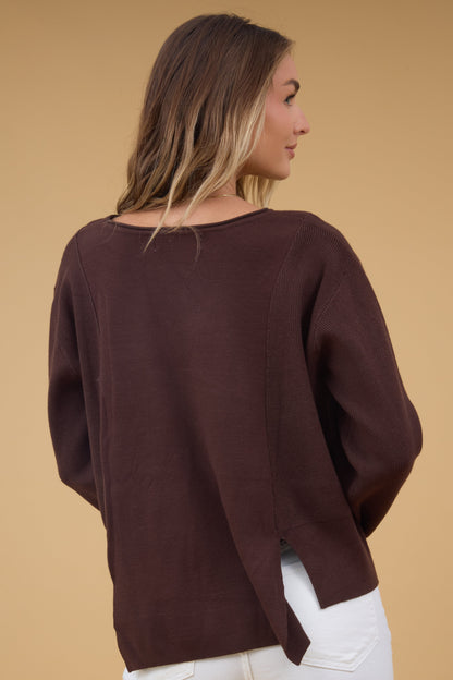 Back view of a woman wearing a loose fittig top with long sleeves and short slits  at the hips.