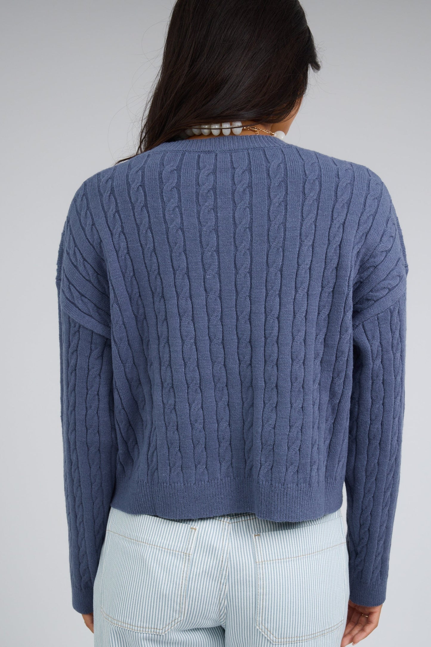 Back view of a woman wearing a blue cable knit sweater with drop shoulders and long sleeves.