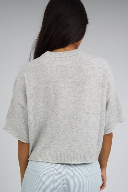 Back view of a woman wearing a loose fitting light grey, lightweight sweater and elbow length sleeves.
