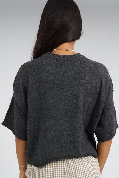 Back view of a woman wearing a charcoal loose fitting, lightweight sweater with loose elbow length sleeves and a round neckline.