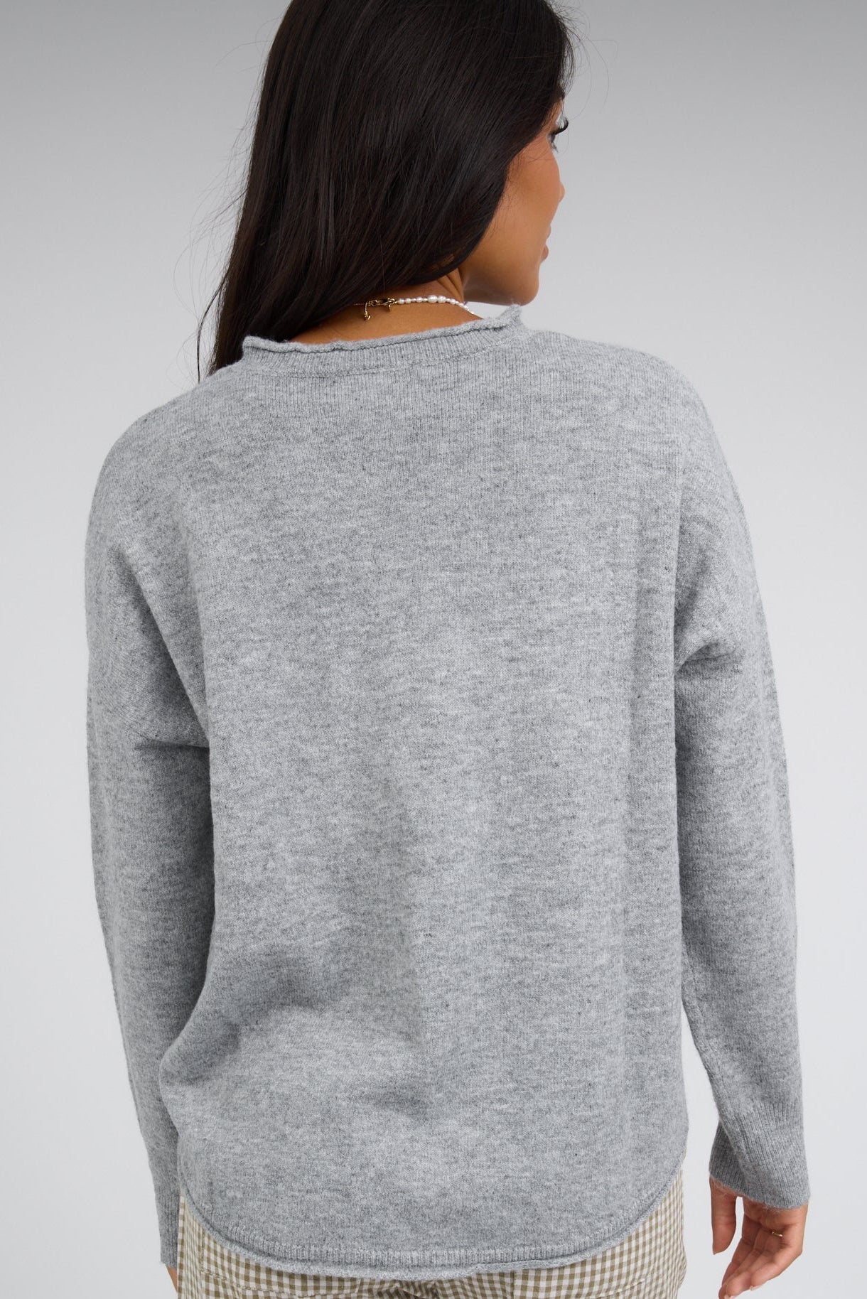 Back view of a young woman wearing a heather grey pullover sweater with long sleeves.
