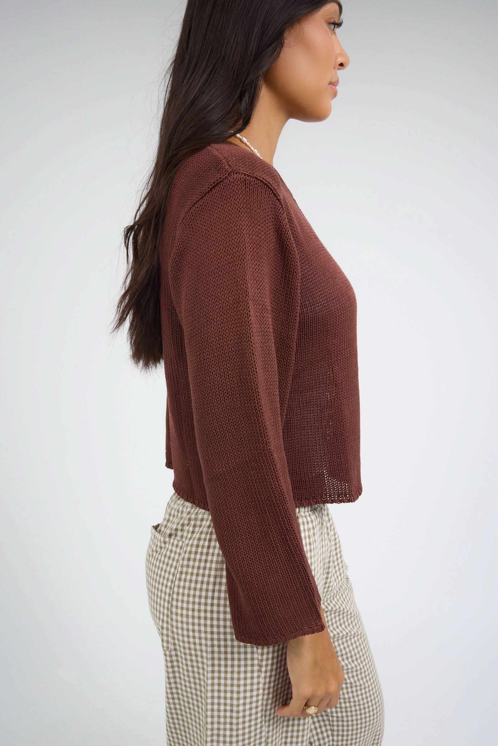 Side view of a woman wearing a loosely knit brown sweater with long sleeves.