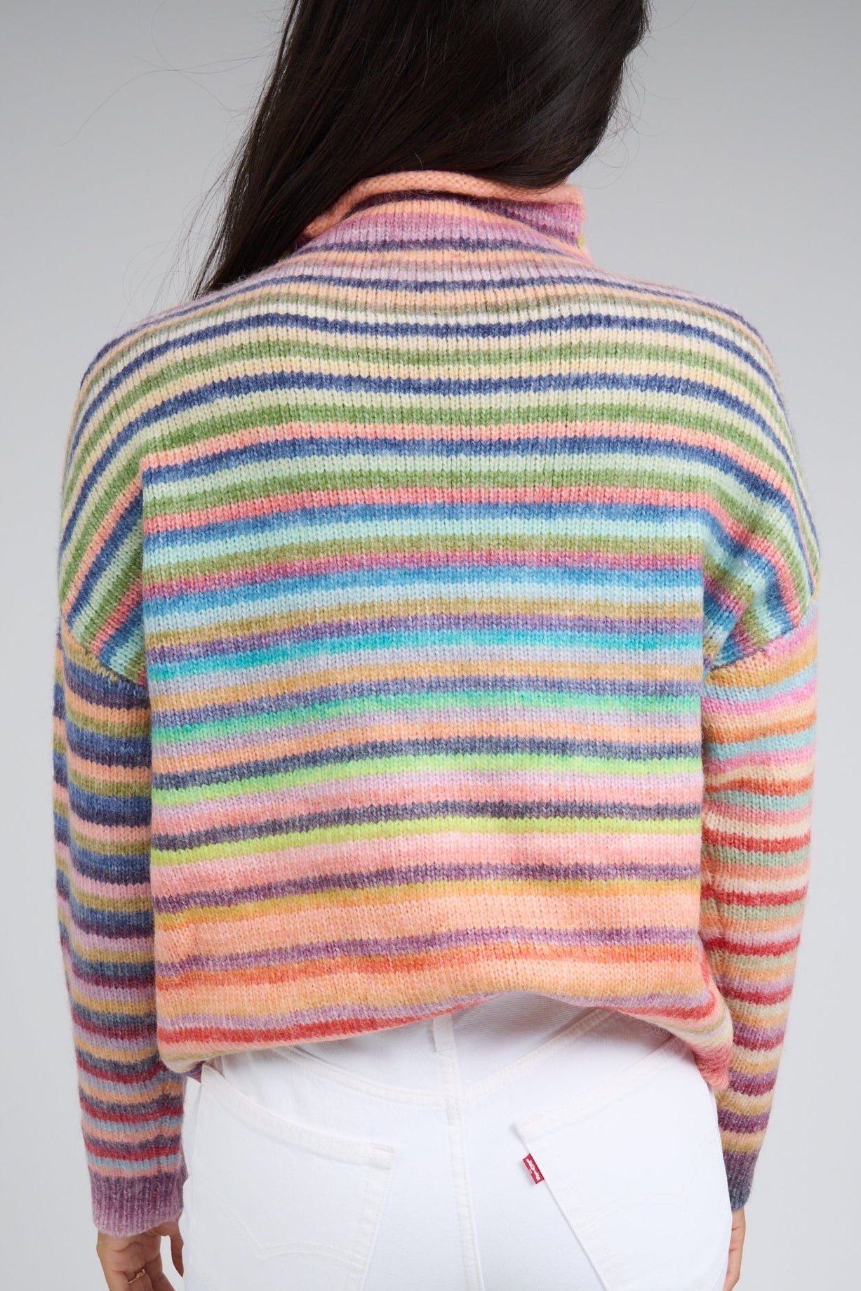 Back view of a woman wearing a rainbow stripe long sleeve sweater.