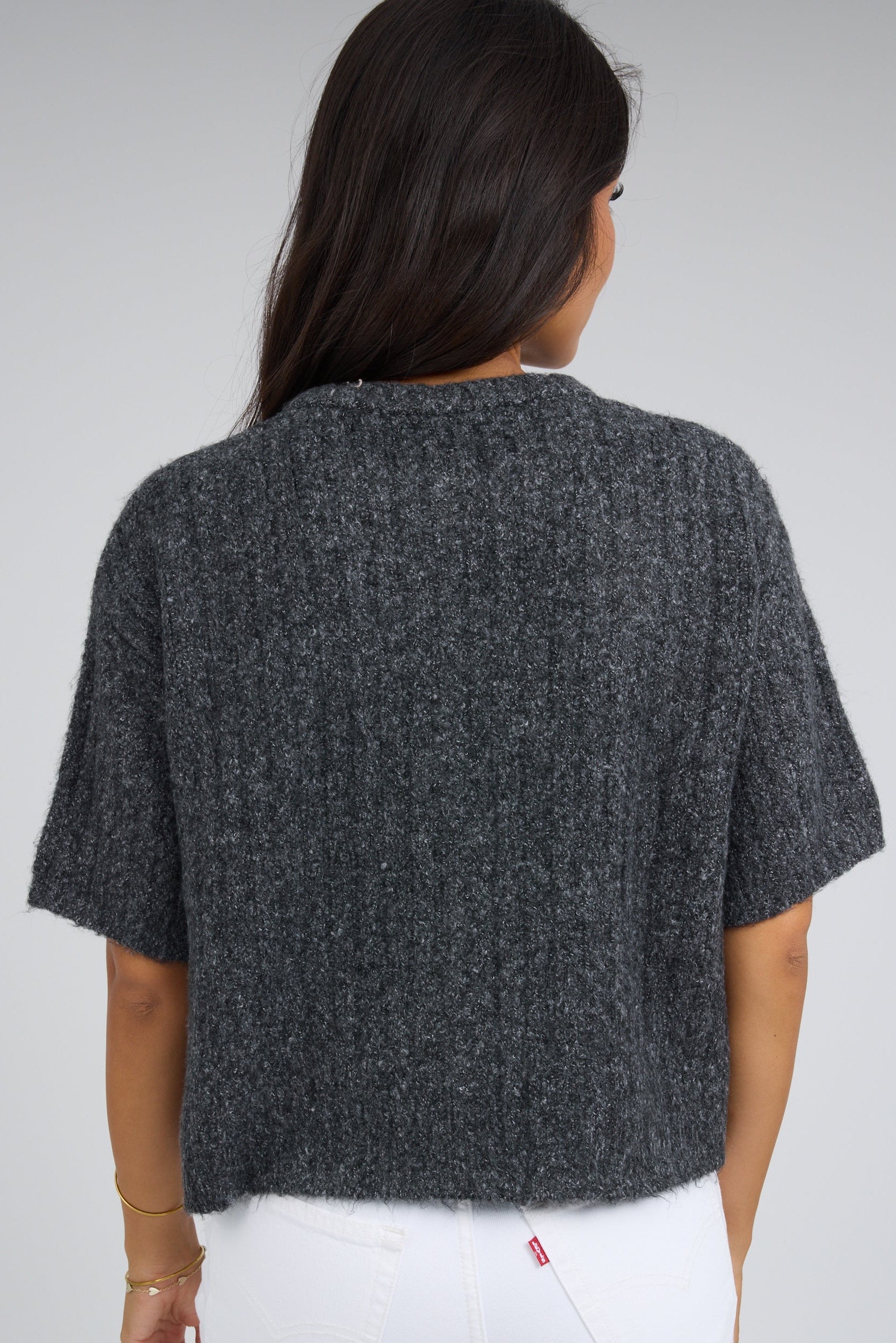 Back view of a young woman wearing a dark grey wide ribbed cardigan with short sleeves.