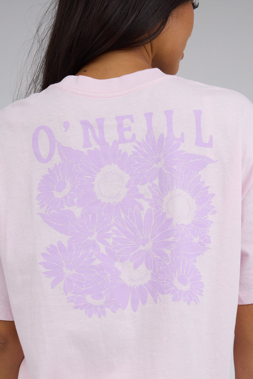 Back view of a woman wearing a light pink graphic tee with a large lavender floral back graphic.