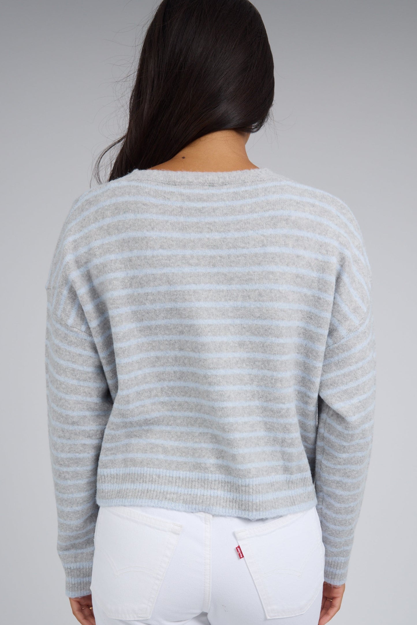 Back view of a woman wearing a grey & light blue stripe cardigan with long sleeves.