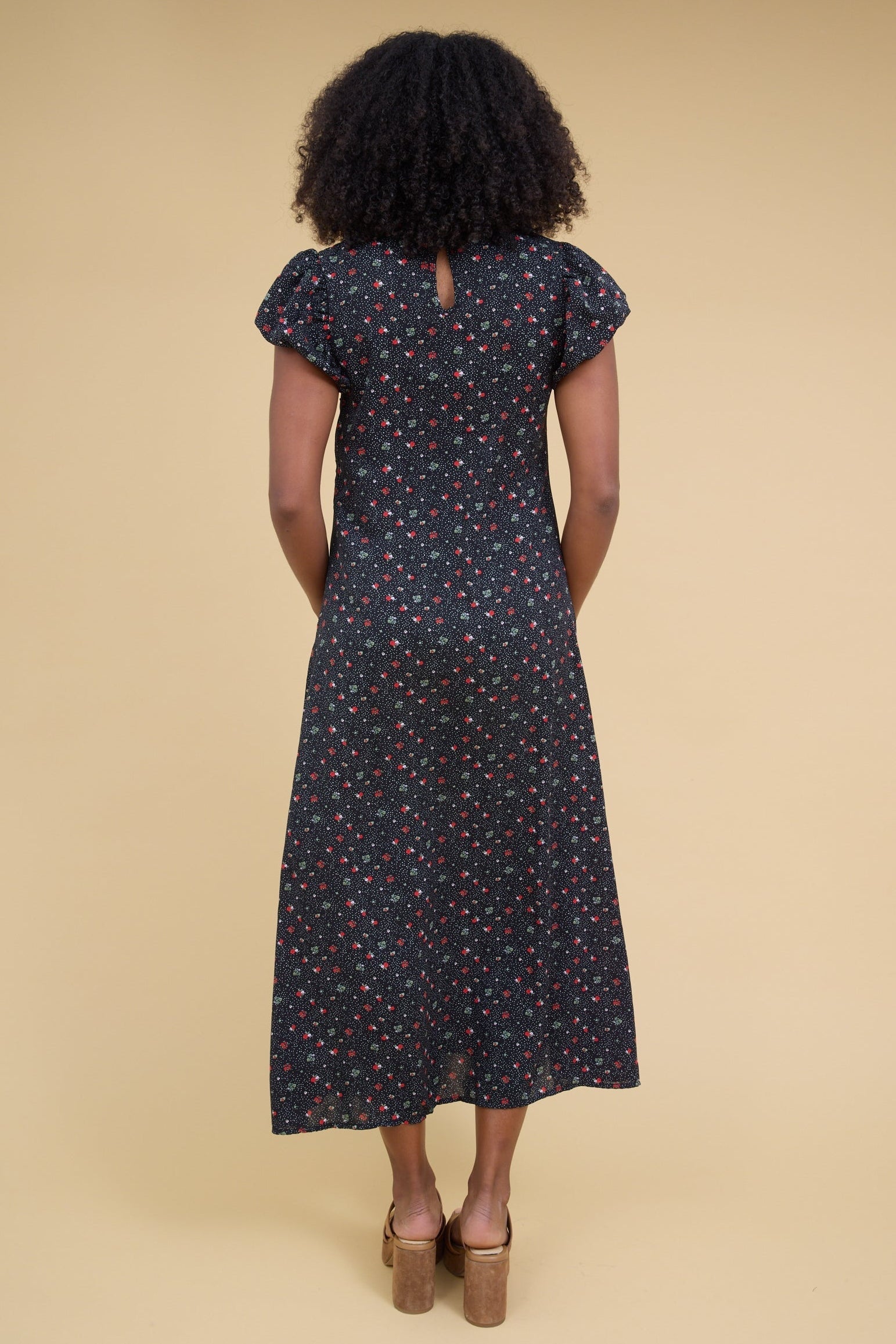 Back view of a woman woman wearing a black floral midi dress with gathered cap sleeves.