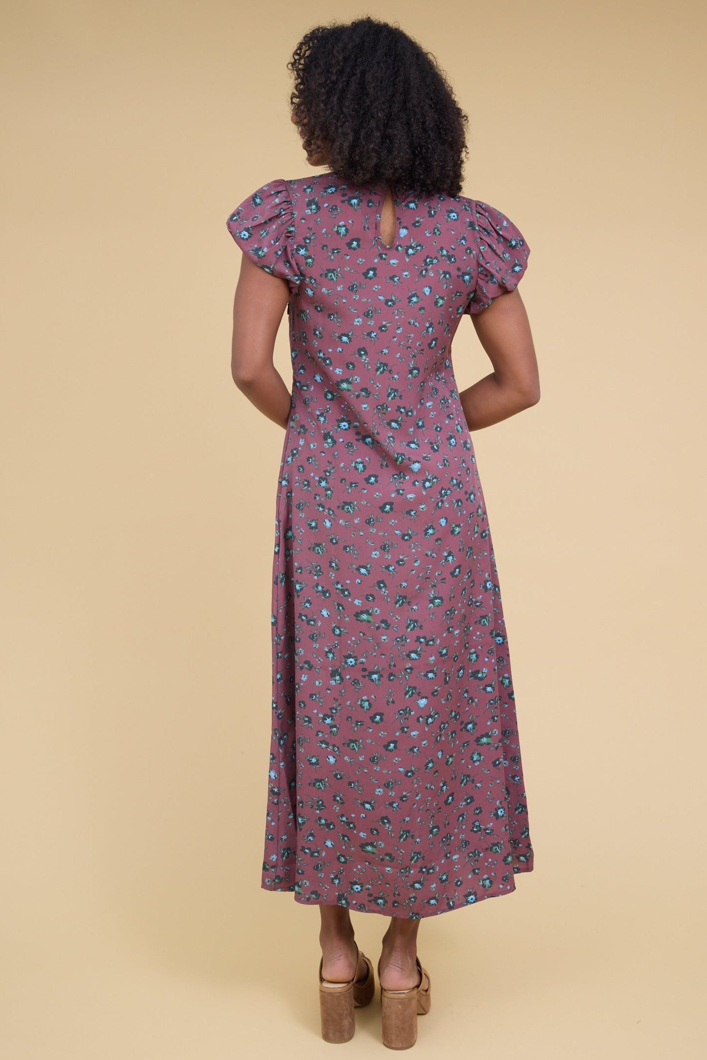 Back view of a young woman wearing a magenta midi dress with gathered cap sleeves.
