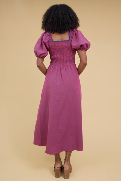 Back view of a woman wearing a red & blue gingham midi dress with a square neckline, balloon sleeves and a smocked bodice.