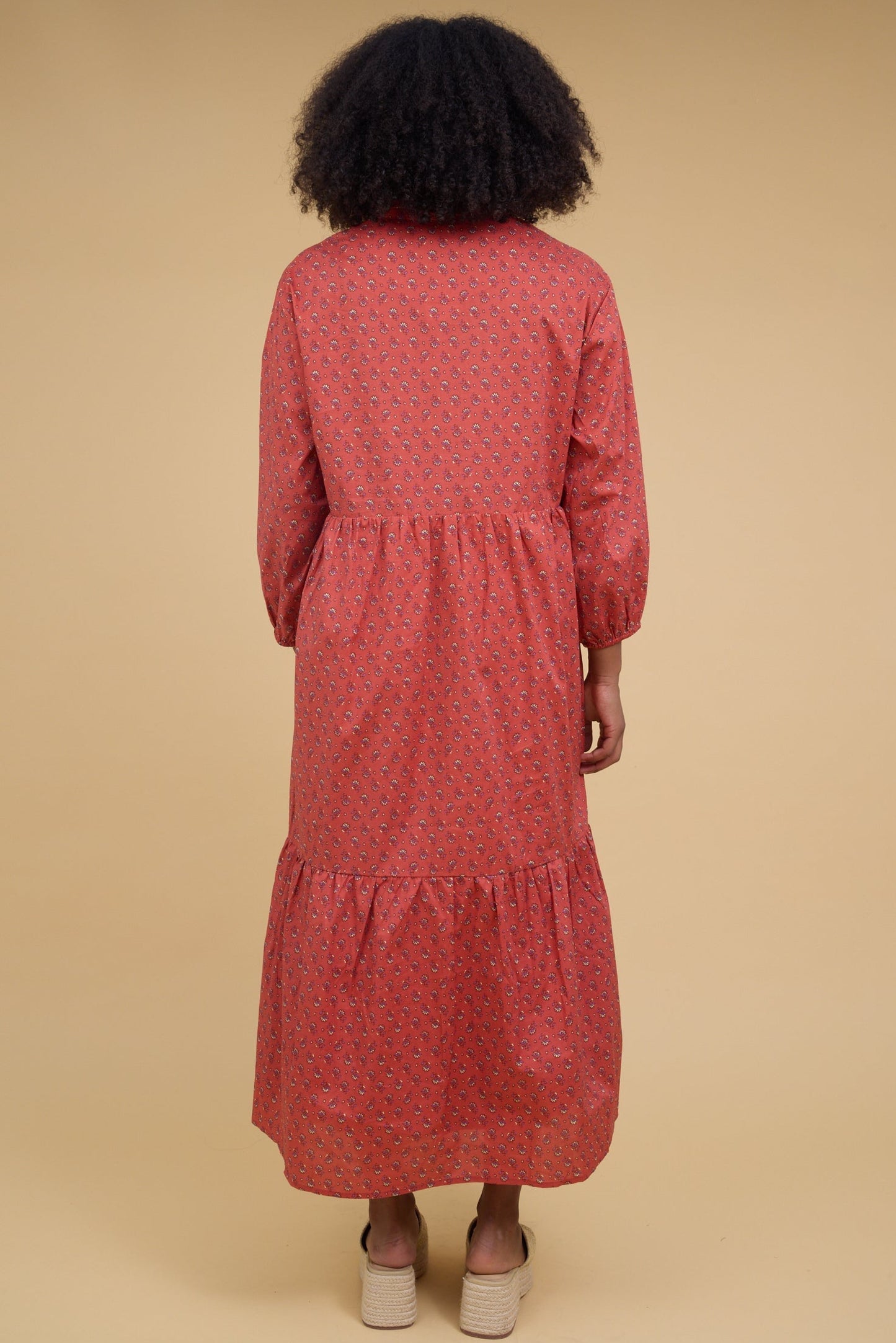 Back view of a young woman wearing a red floral midi dress with long sleeves and a wide bottom ruffle.