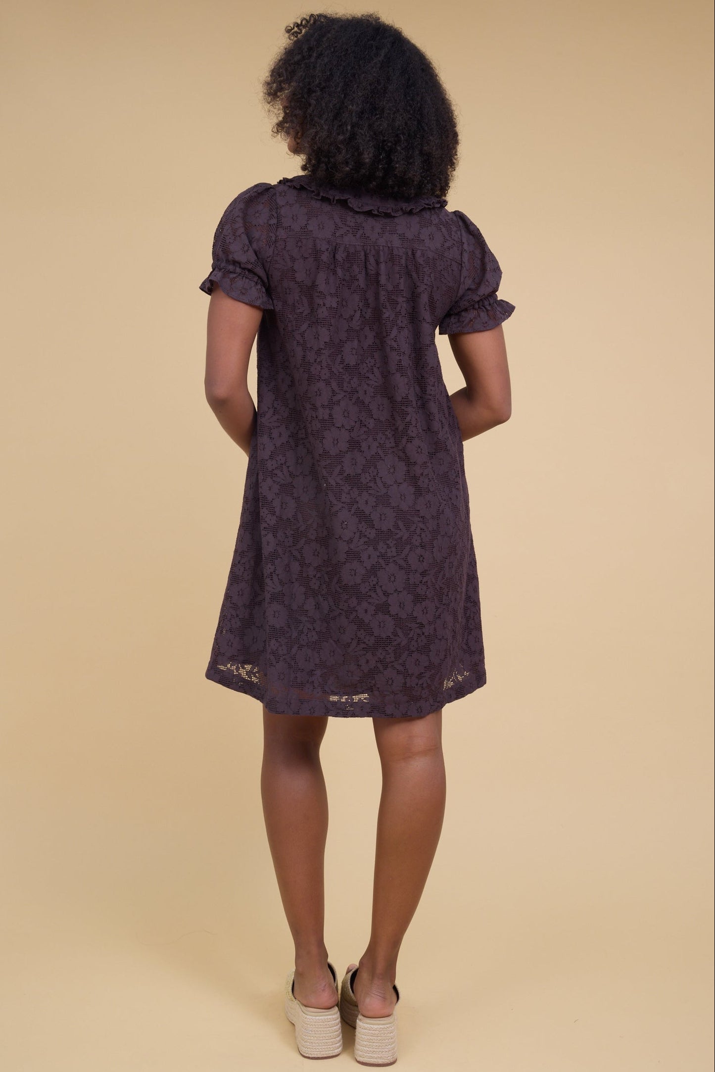 Back view of a woman wearing an all  lace brown short dress with puff sleeves.