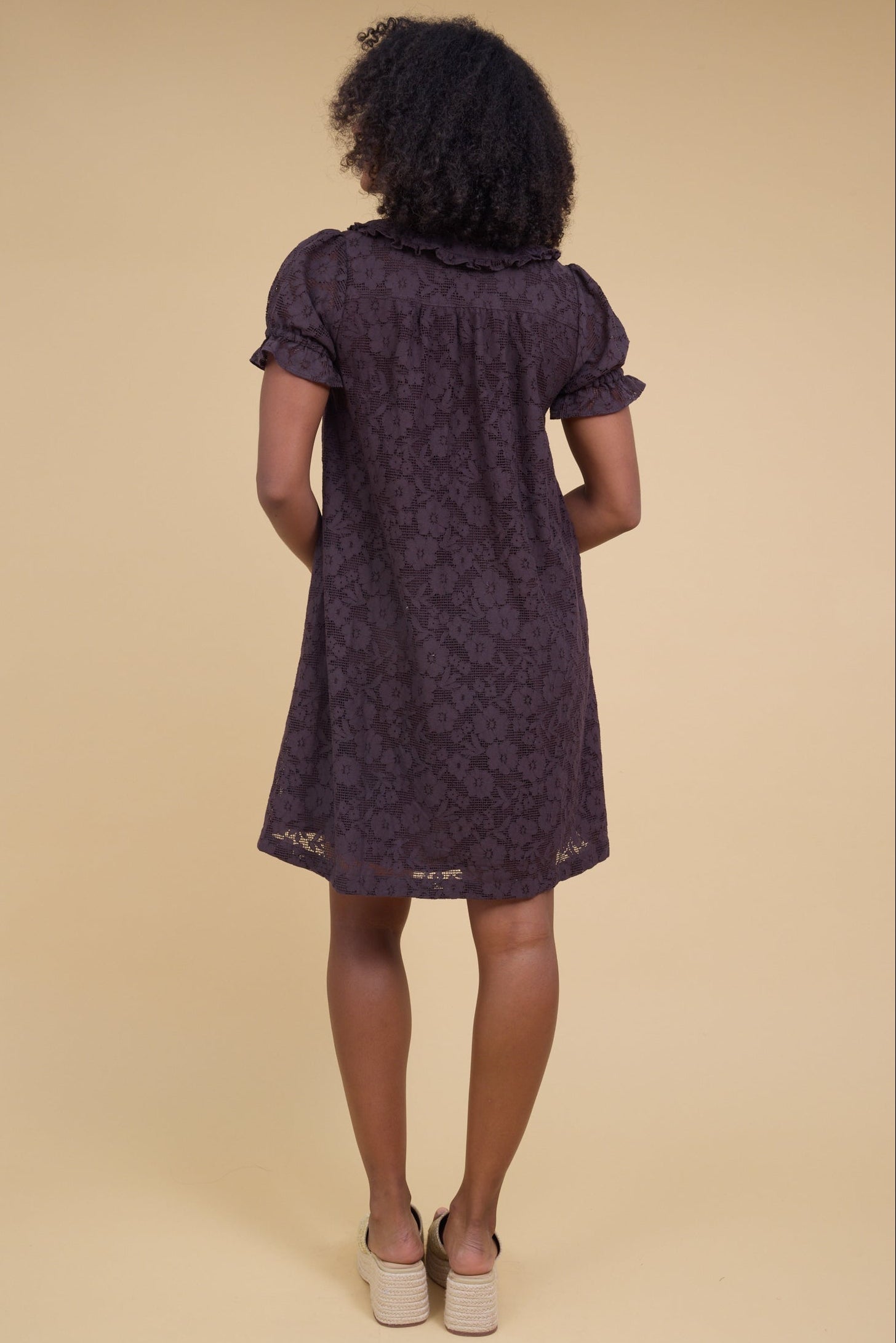 Back view of a woman wearing an all  lace brown short dress with puff sleeves.