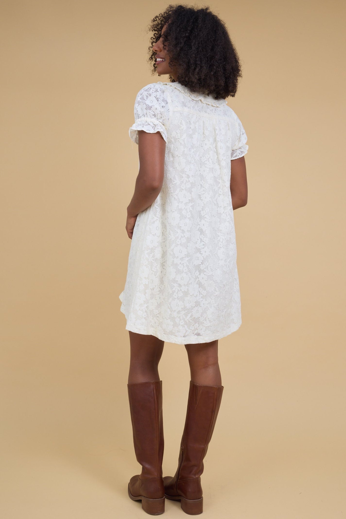 Back view of a woman wearing an off white all lace midi dress with ruffle cuff puff sleeves.