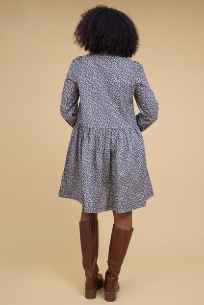 Back view of a woman wearing a charcoal floral print short dress with long sleeves.