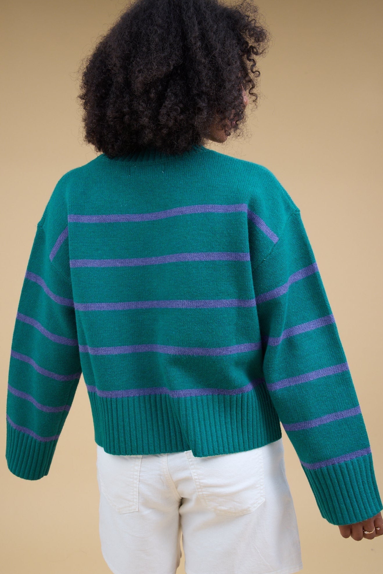 Back view of a woman wearing a green sweater with blue stripe and long sleeves.