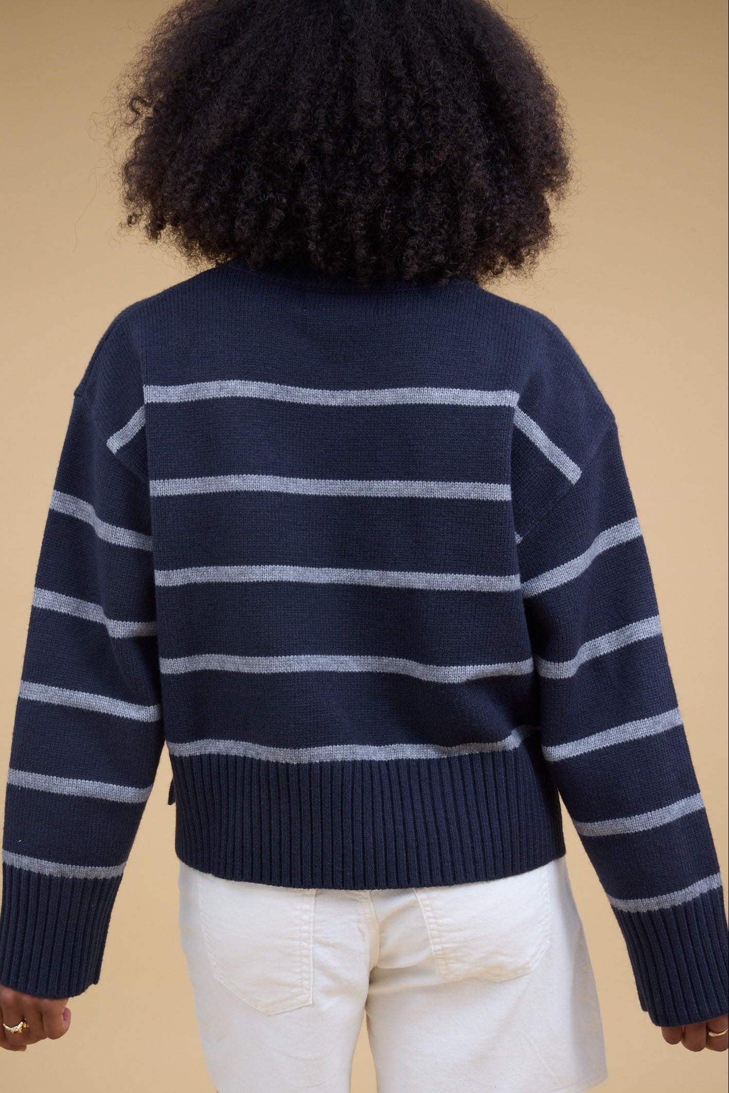 Back view of a woman wearing a navy and grey pullover sweater with wide biggind at the cuffs & waist.