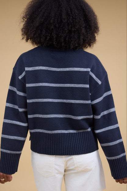 Back view of a woman wearing a navy and grey pullover sweater with wide biggind at the cuffs & waist.