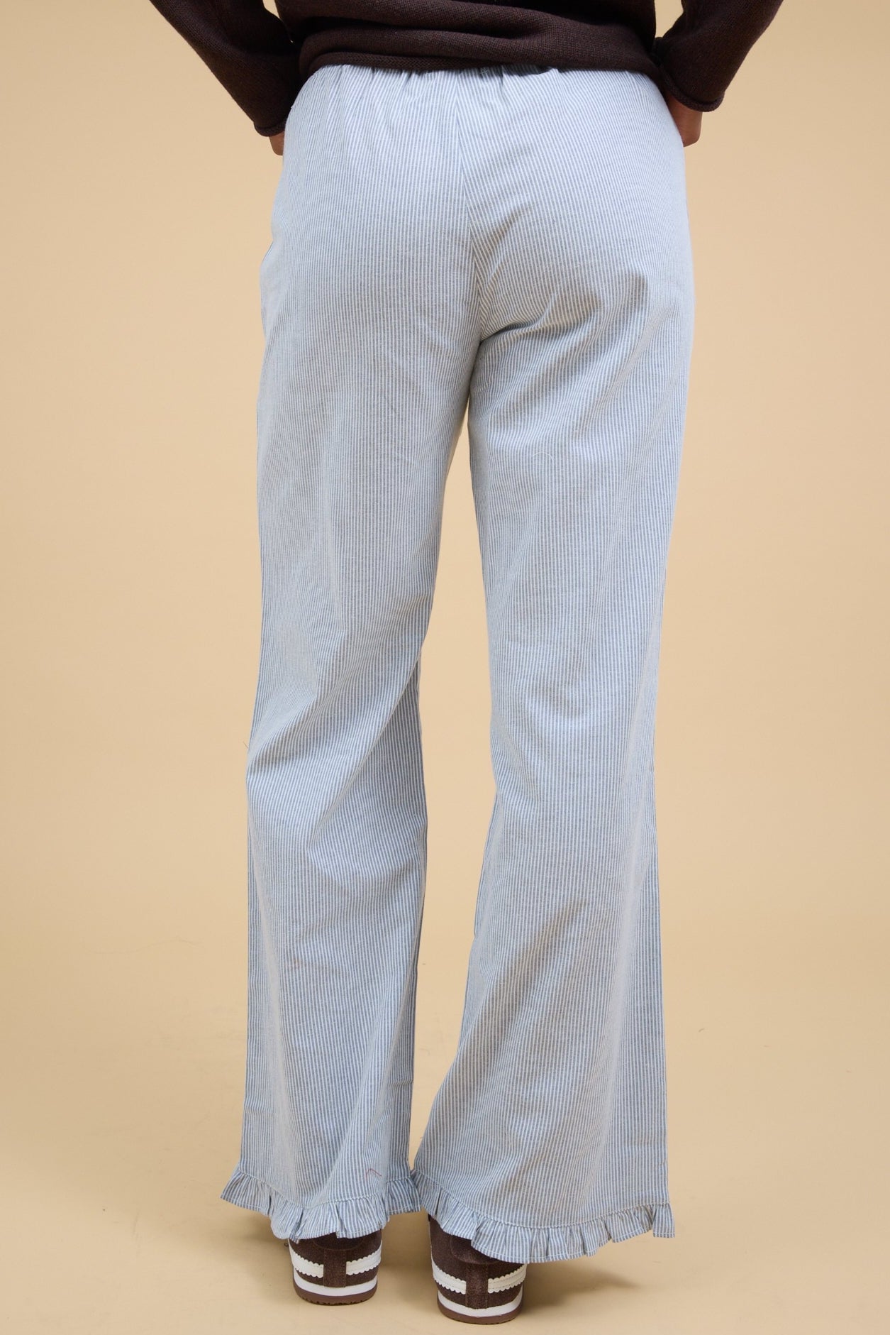 Back view of a woman wearing a pair of navy & white pinstripe pant with a narrow ruffle hem.