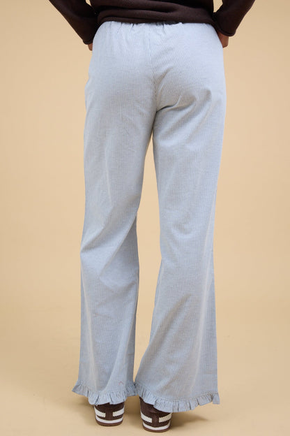 Back view of a woman wearing a pair of navy & white pinstripe pant with a narrow ruffle hem.