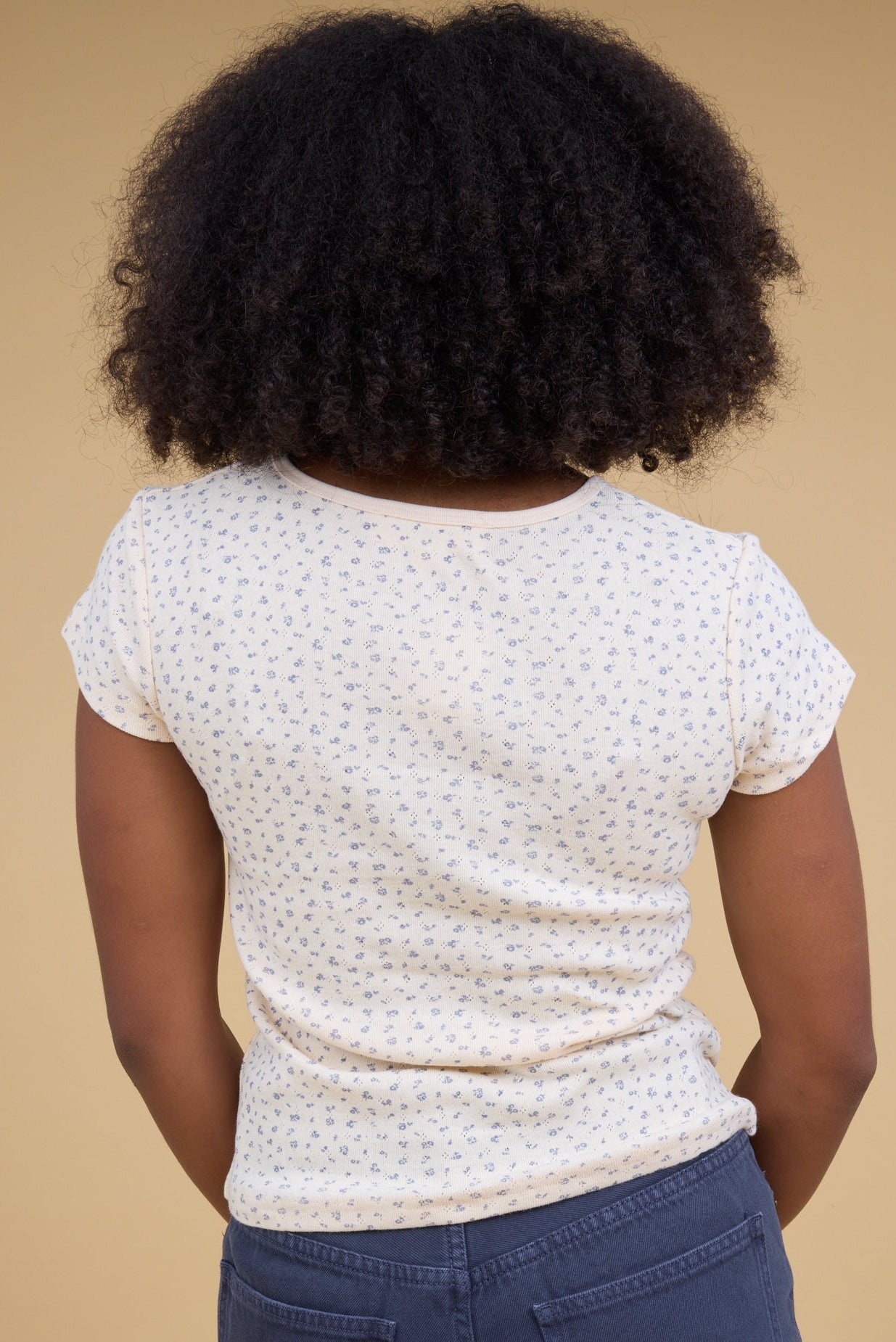 Back view of a woman wearing a close fitting rib knit tee with short sleeves.
