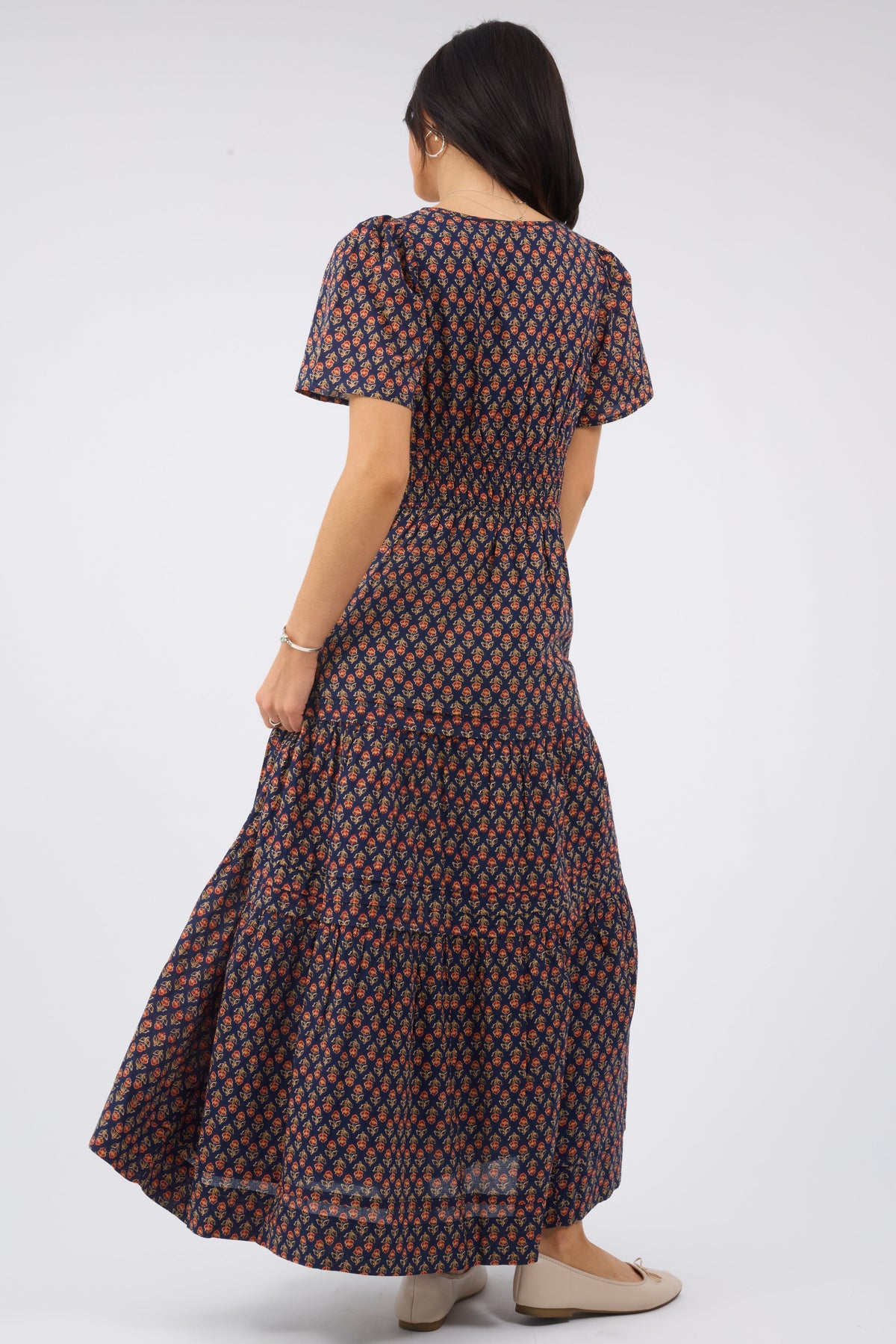 Back view of a woman wearing a navy & red floral print midi dress with short sleeves, wide elastic waistband and a full tiered skrit.