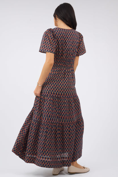 Back view of a woman wearing a navy & red floral print midi dress with short sleeves, wide elastic waistband and a full tiered skrit.